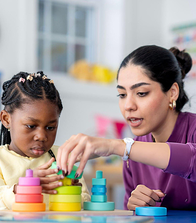 Teacher helping a young student with classroom learning materials